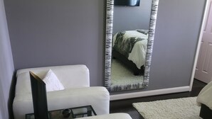 A hotel room with a large mirror, a white sofa, a patterned throw pillow, and a small table with a glass top. - Serene Adult-Only Suite in the Heart of Houston (Houston)