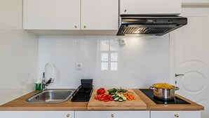 Une cuisine moderne avec des meubles blancs, un évier en acier inoxydable, un plan de travail en bois, une planche à découper avec des légumes et une casserole sur une plaque de cuisson à induction.