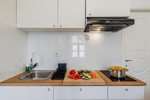 A modern kitchen with white cabinets, a stainless steel sink, a wooden countertop, a cutting board with vegetables, and a pot on an induction cooktop.