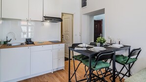 A compact kitchen with white cabinets, a wooden countertop, and a black dining table with green cushioned chairs.