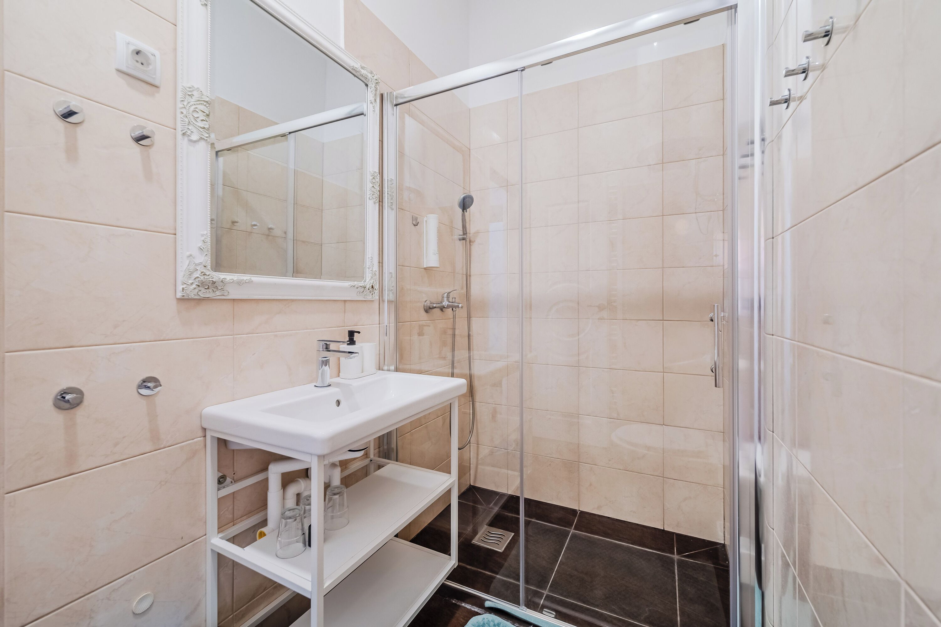 Une salle de bain moderne avec une douche à parois de verre, un lavabo blanc et un miroir doté d’un cadre orné.