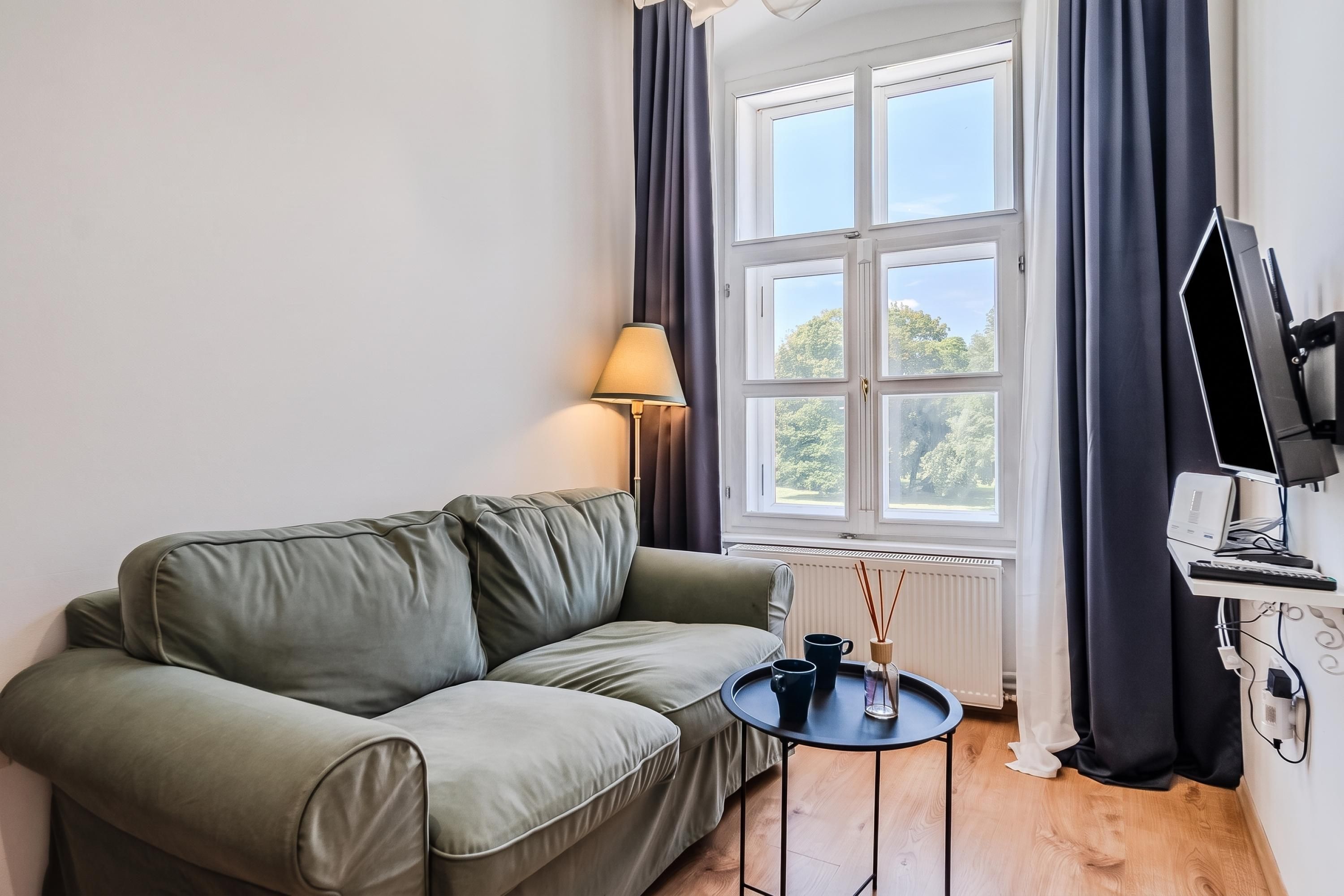 A room with a sofa, a small table, a lamp, a TV, and a window with curtains.