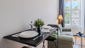 Een eethoek met een tafel voor twee, een potplant en uitzicht op het buitenleven door een raam.