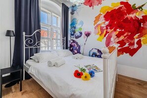 A neatly made bed with white linens, a black nightstand, and a wall with a floral mural. - Old Town Heritage Suite 2, Osijek, Croatia (Osijek)