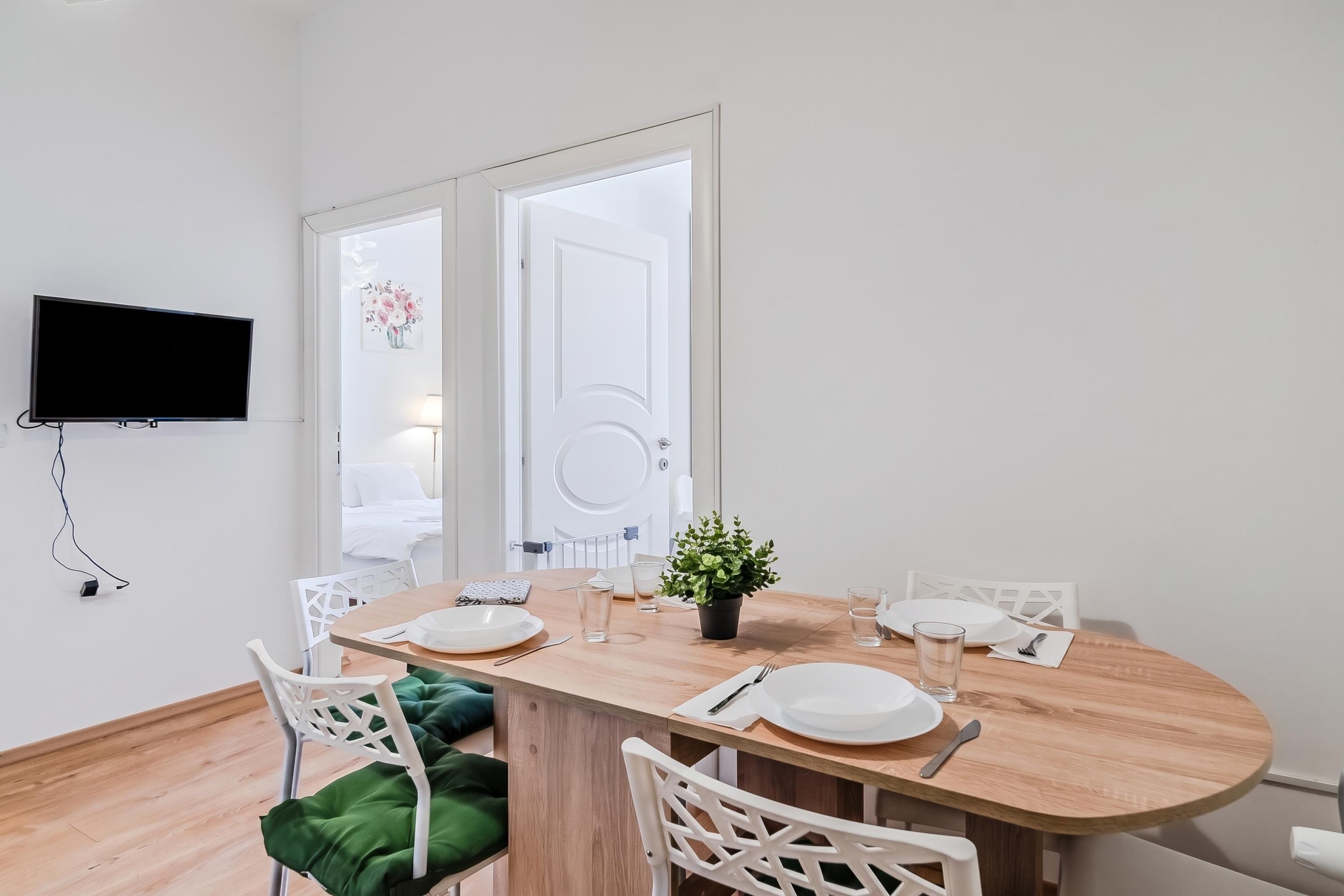 Un coin repas avec une table en bois, des chaises blanches et un téléviseur à écran plat fixé au mur.