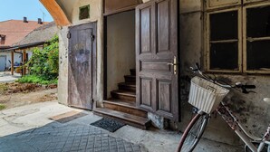 Eine Treppe führt zu einer Holztür, ein Fahrrad mit Korb und ein Fenster mit Blick auf ein Gebäude mit rotem Dach.