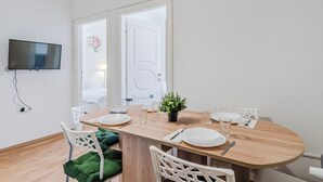 Ein Essbereich mit einem Holztisch, weißen Stühlen und einem an der Wand befestigten Fernseher.