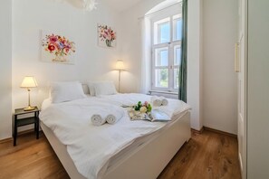 A neatly made bed with white linens, a bedside lamp, and a window with curtains.