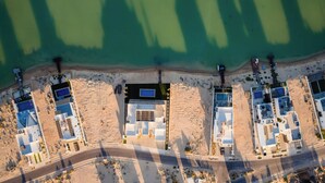 Ett flygbildsbild av ett hotell vid kusten med flera byggnader, en sandstrand och fri utsikt över havet.