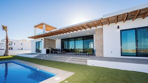 Ett modernt hus med en swimmingpool, utomhusmöbler och en pergola.