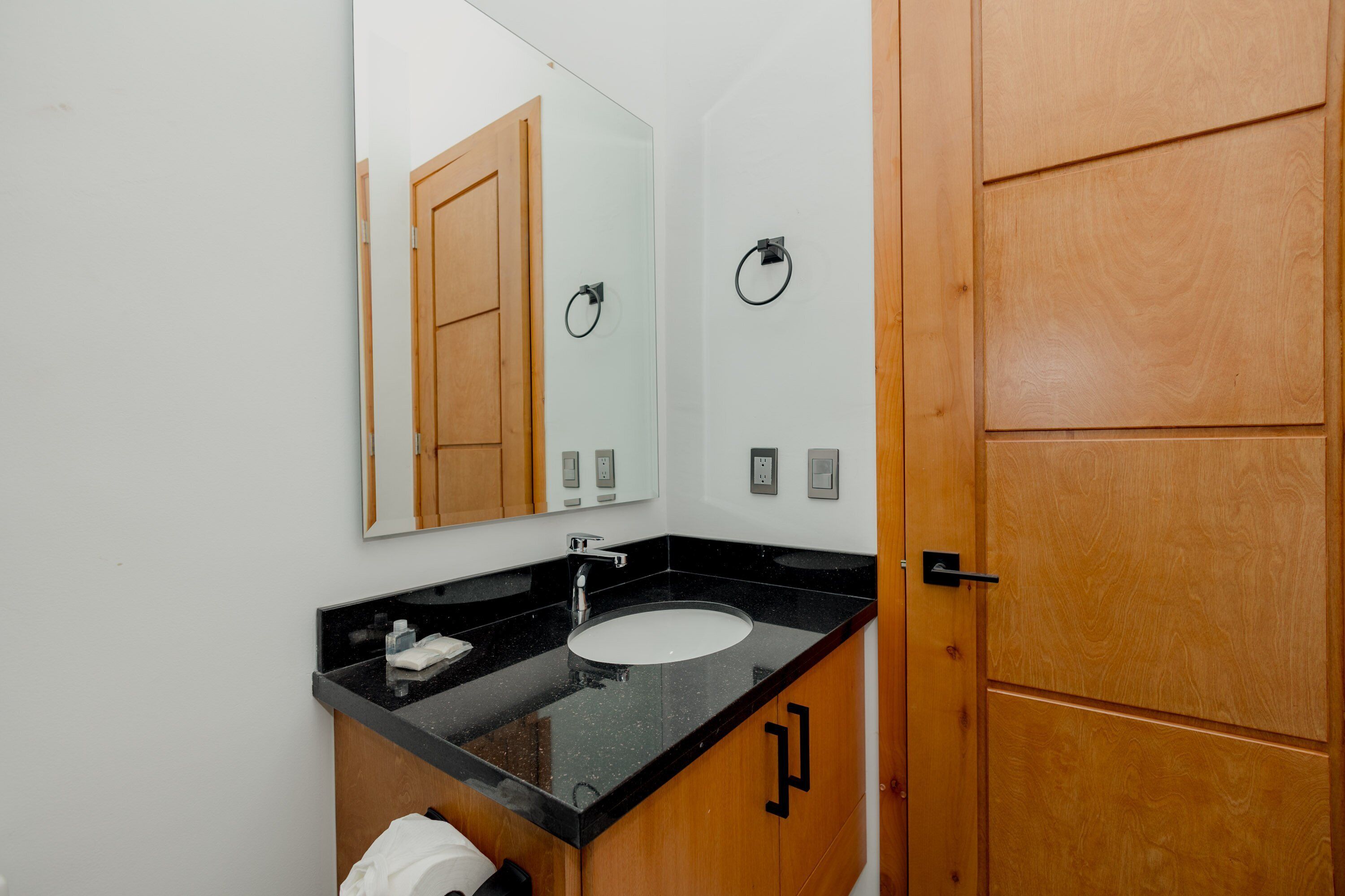 A bathroom with a black countertop sink, a mirror, and wooden cabinets.