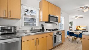 Una cocina moderna con armarios de madera, electrodomésticos de acero inoxidable, un lavamanos doble y una zona de comedor con televisor.