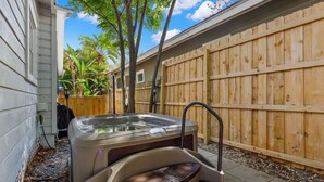 Un jacuzzi en un patio trasero con una valla de madera y una casa al fondo.