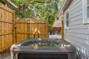 A hot tub in a backyard with a wooden fence and a house in the background.