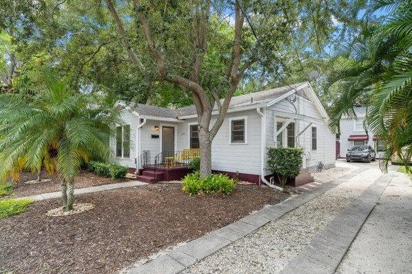 A single-story house with a front porch, a small yard with mulch, and a palm tree.