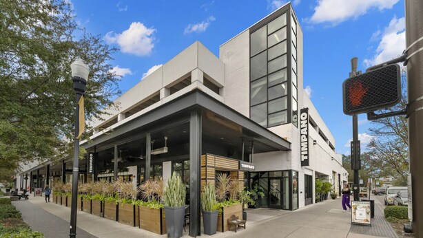 Un edificio moderno con fachada de vidrio extensa, área de estar al aire libre y entrada visible.