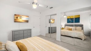 Un dormitorio con cama, cómoda, ventilador de techo, espejo grande y obras de arte en las paredes.