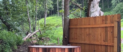 A hot tub on a wooden platform with a wooden fence and trees in the background.