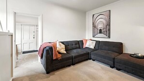 Una sala de estar moderna con un sofá modular, una obra de arte enmarcada en la pared y una puerta que da a otra habitación.