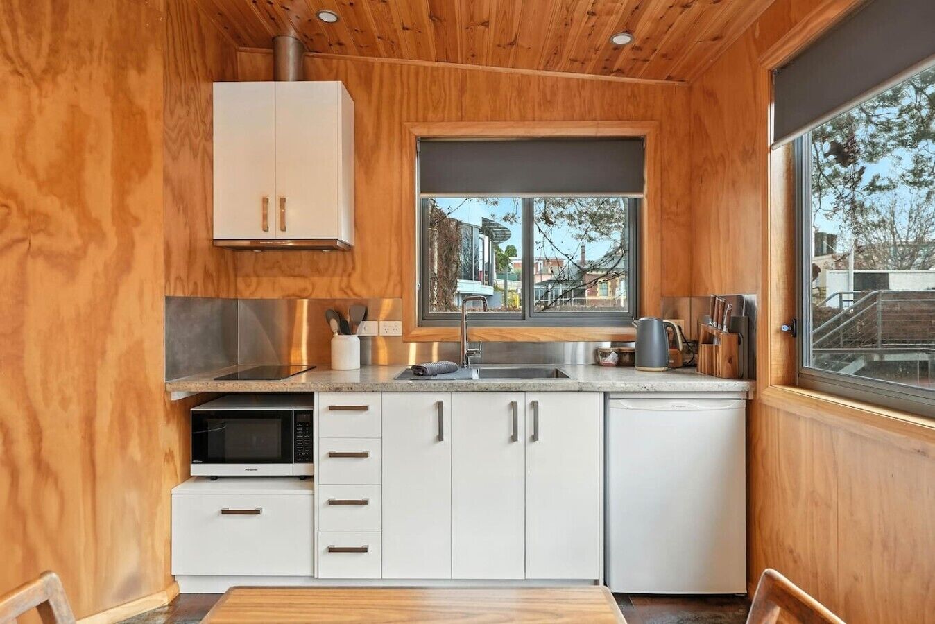 Eine kleine Küche mit Holzwänden, einem Fenster und Blick ins Freie.