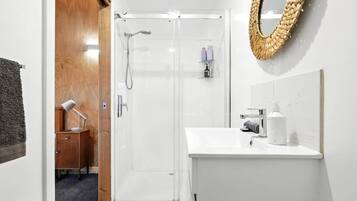 A modern bathroom with a glass shower enclosure, a white sink with a mirror, and a wooden cabinet.
