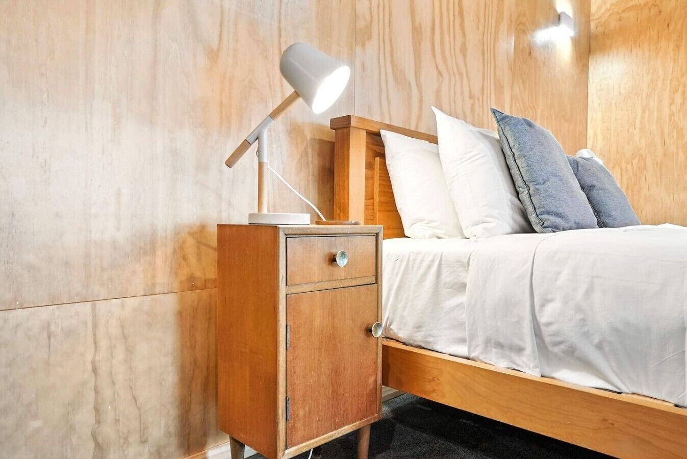 A wooden bed with white bedding and a nightstand with a lamp.