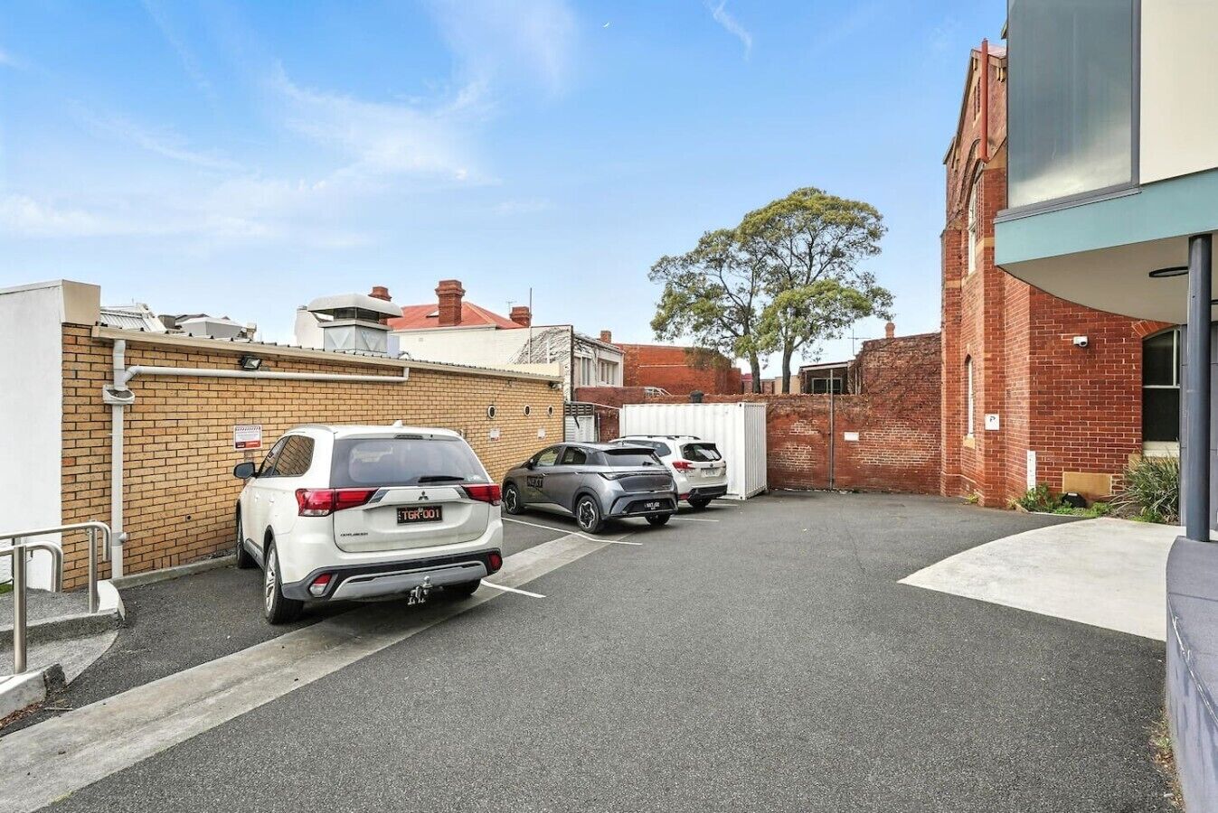 A parking area with cars, a brick wall, and a building with a flat roof.