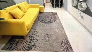 Una sala de estar moderna con un sofá amarillo, un tapete estampado y una escalera que lleva a un comedor.