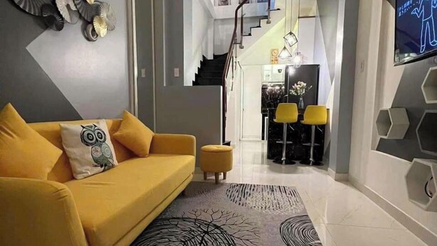 Una sala de estar moderna con un sofá amarillo, un tapiz estampado y una escalera que lleva a una zona de cocina.