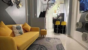 Una sala de estar moderna con un sofá amarillo, un tapiz estampado y una escalera que lleva a una zona de cocina.
