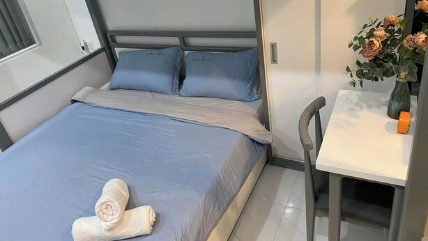 Una cama bien hecha con ropa de cama y almohadas azules, una mesita con un florero y una silla.