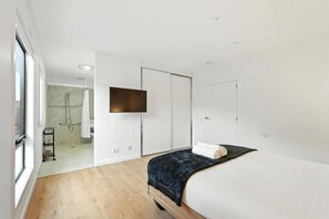 A modern bedroom with a bed, a TV mounted on the wall, and a walk-in closet.