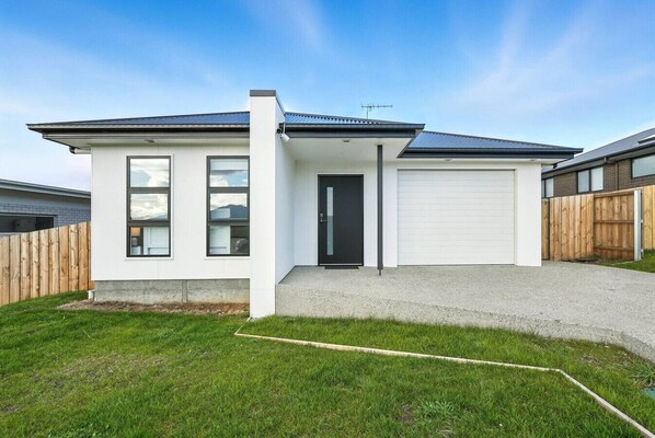 A modern two-story house with a garage, a front door, and a fenced backyard.