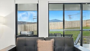 A black leather sofa with a single cushion, positioned in front of a sliding glass door leading to an outdoor patio area with a wooden fence and a grill. - Modern & Accessible | Old Beach (Old Beach)