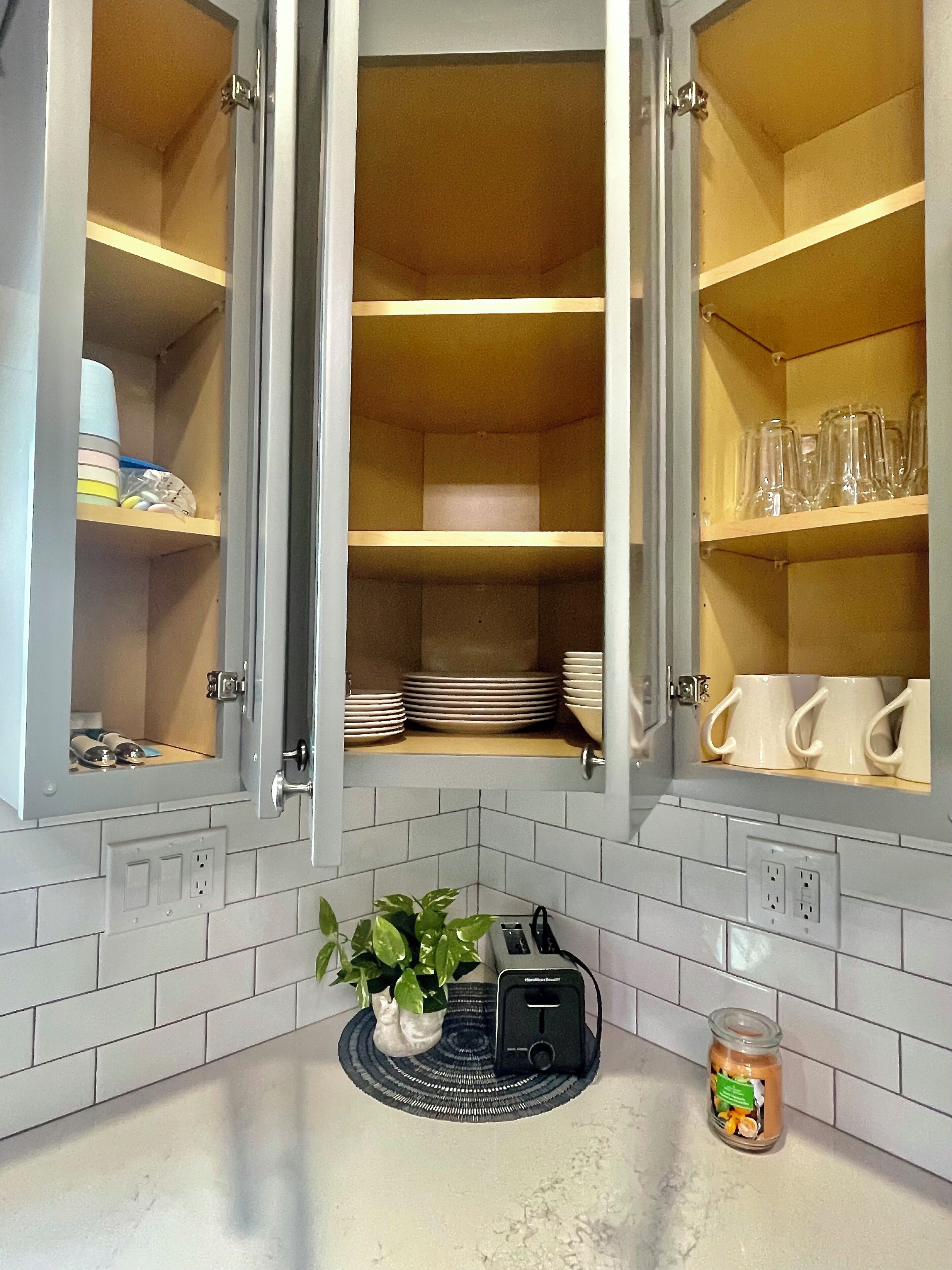 A kitchen with open cabinets, a toaster, a plant, and a jar of peanut butter on the counter.