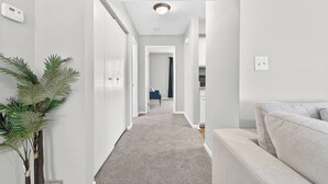Un pasillo con alfombra gris, paredes blancas, una planta y una silla azul.
