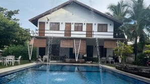 Una piscina con chorros de agua, rodeada por un edificio con balcón y vistas a palmeras.