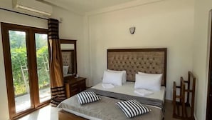 Un dormitorio amplio con una cama grande, ventilador de techo y vistas a la vegetación a través de la puerta corredera de cristal.
