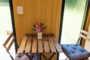 A small wooden table with a vase of flowers, two chairs, and a window with a view of the outdoors.
