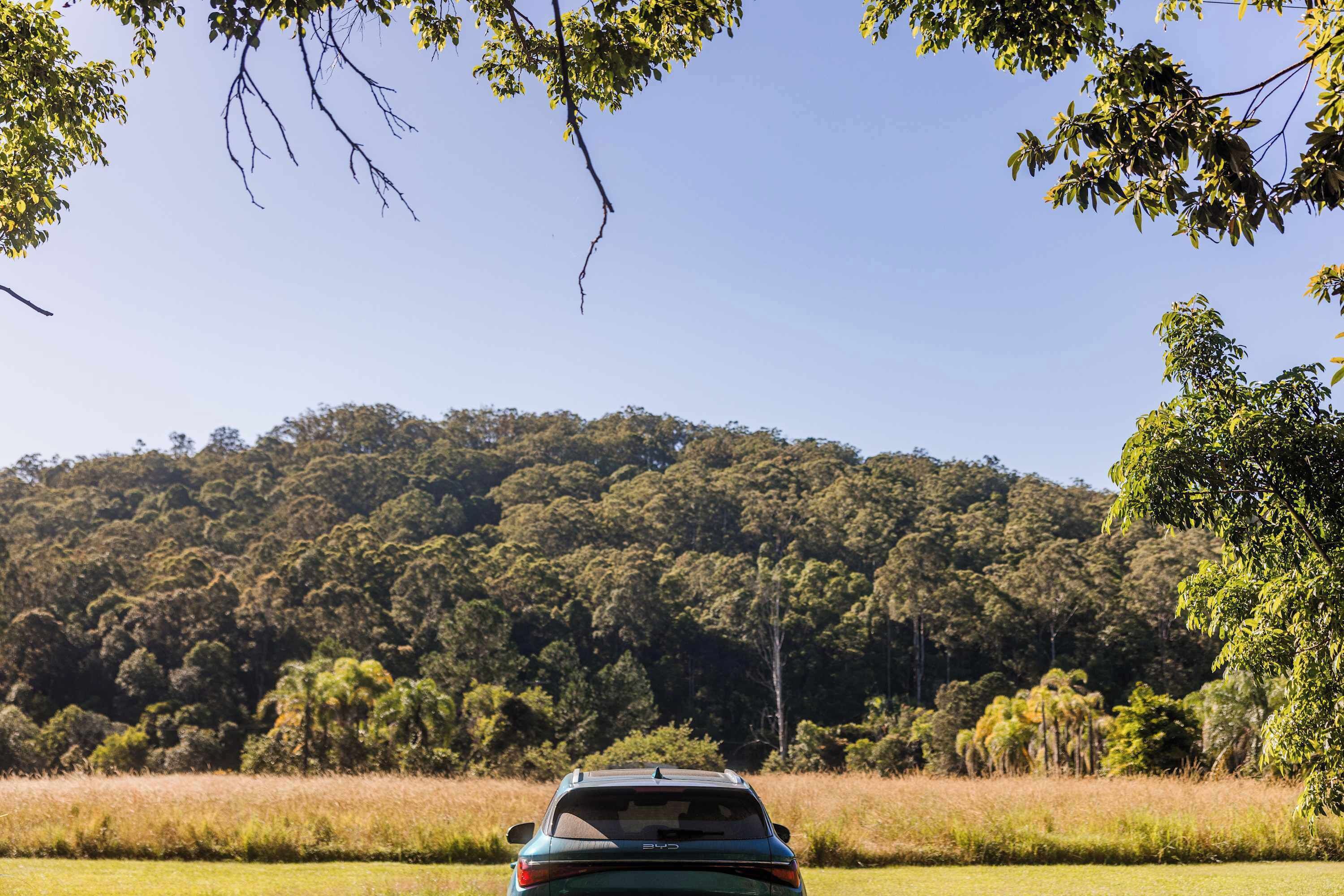 A car parked in a field with a forested hill in the background.