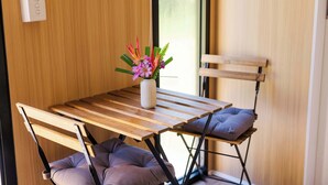 Ein Holztisch mit einer Blumenvase, zwei Stühle mit Kissen und ein Fenster mit Jalousien.