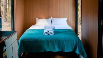 Un letto rifatto con cuscini bianchi e una coperta color petrolio, un asciugamano piegato e un tavolino con un telecomando.