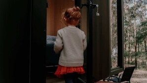Niño en una habitación con piso de madera, un banco y una ventana que da a árboles.