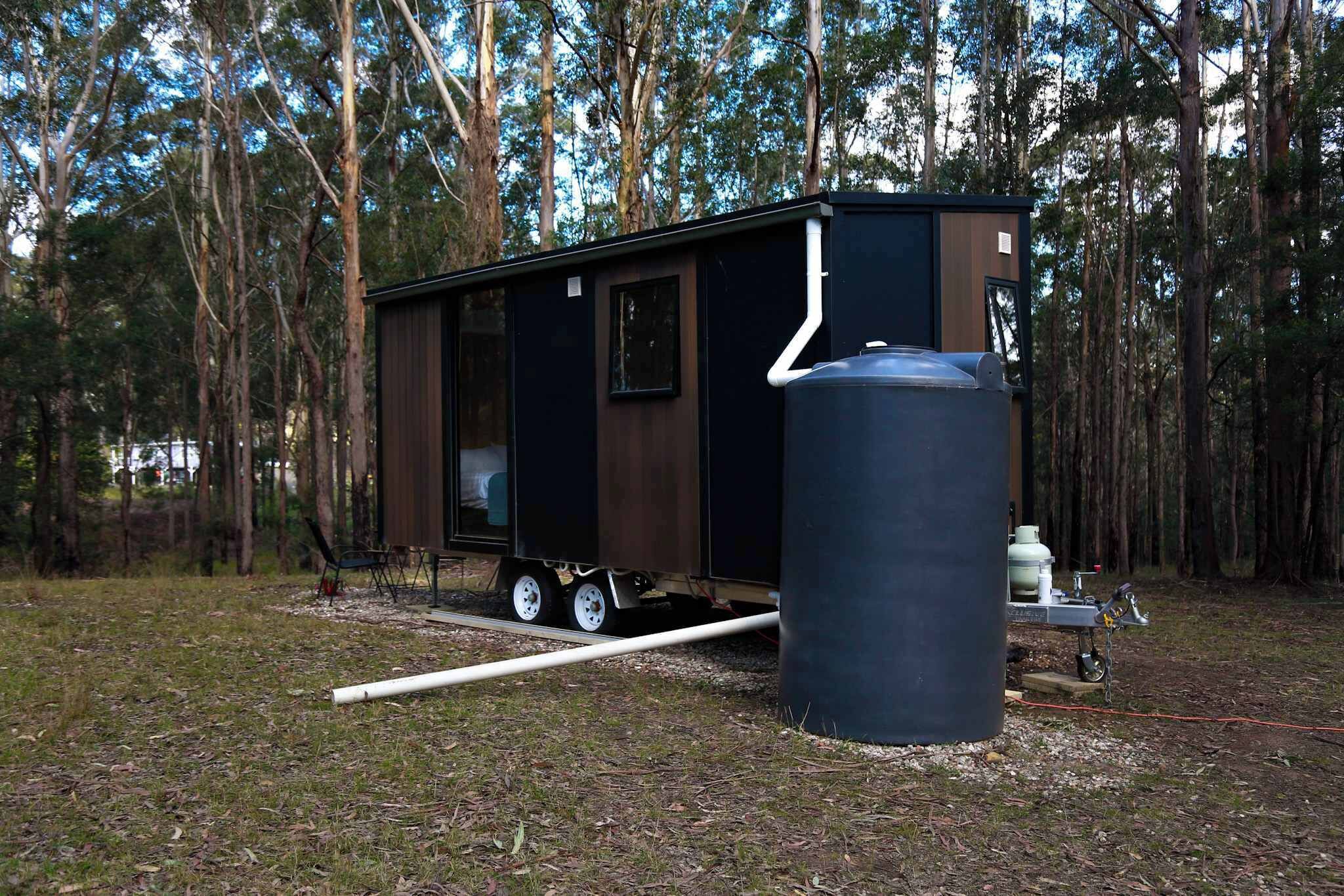 Eine kleine, transportable Hütte mit großem Wassertank, umgeben von Bäumen.