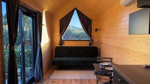 A cozy cabin interior with a sofa, dining table, and large windows offering a view of trees and mountains. - Monteleone 1 by Tiny Away (Battipaglia)