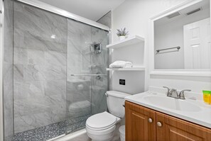 A modern bathroom with a glass-enclosed shower, a white toilet, a wooden vanity with a sink, and a mirror above the vanity.