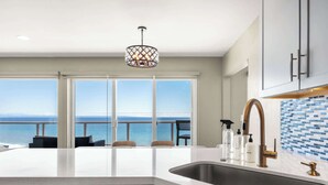 A kitchen with a large island, a stainless steel sink, and a view of the ocean.