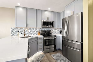 A modern kitchen with grey cabinets, stainless steel appliances, and a tiled backsplash.