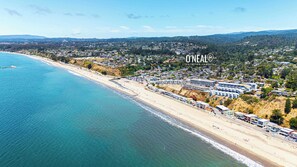 An aerial view of a coastal town with a beach, houses, and a large building complex.