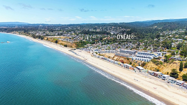 Vista aérea de uma cidade costeira com praia, casas e um grande complexo de edifícios.